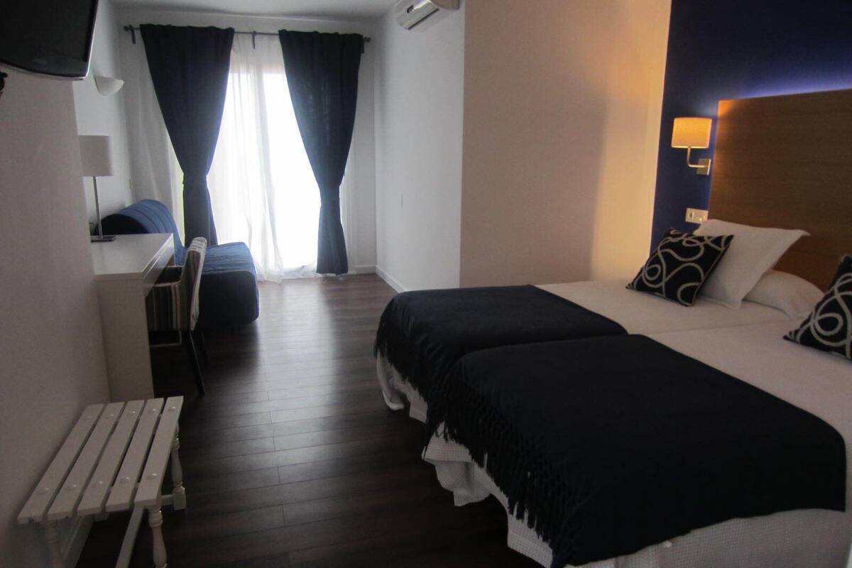 A hotel room with two beds, a desk, a chair, and a small table.