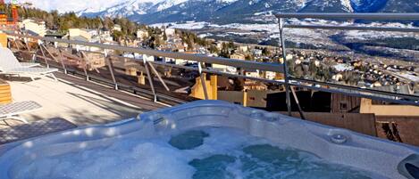 A hot tub with a mountain view, a balcony, and a town in the background.