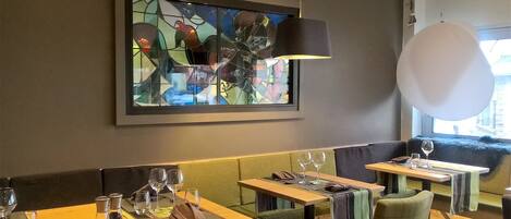A restaurant interior with a stained glass artwork, wooden tables, cushioned seating, and a hanging light fixture.