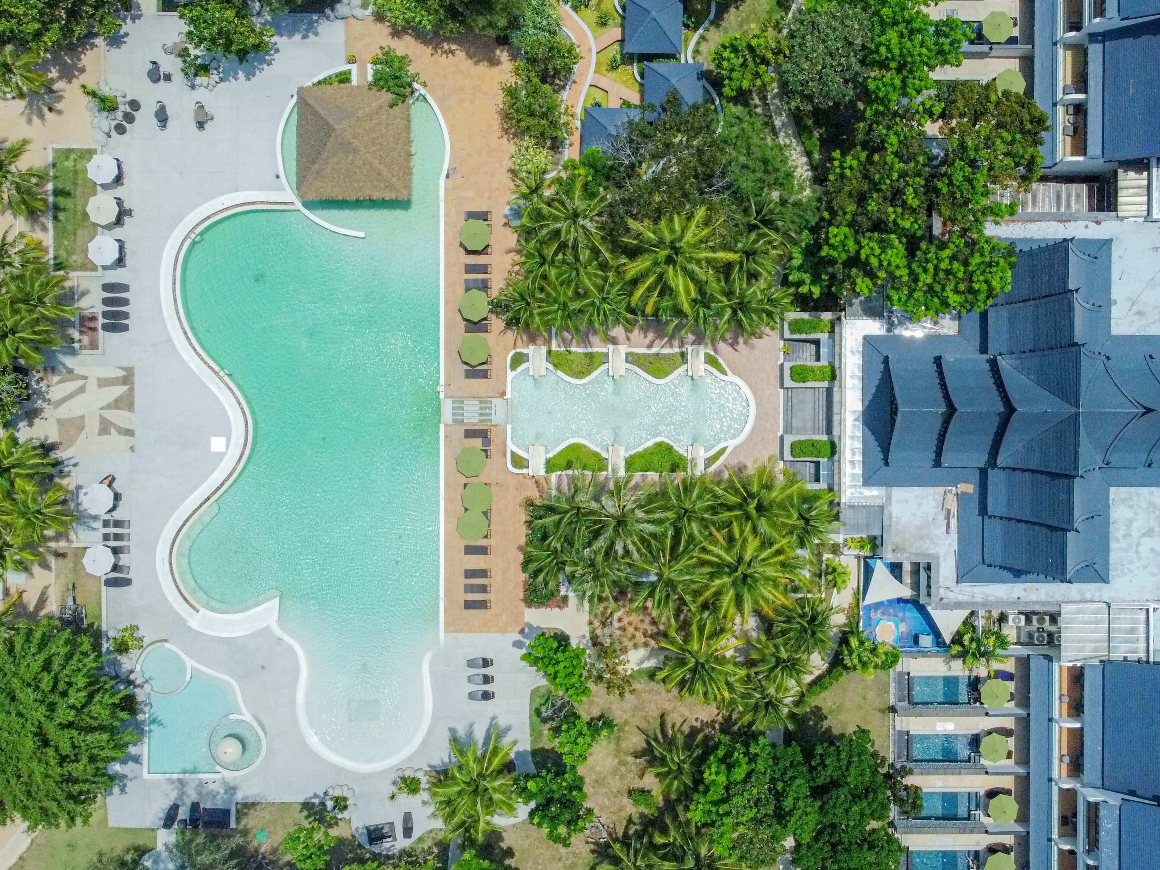 An aerial view of a resort with a large central pool, multiple smaller pools, and a variety of outdoor seating areas surrounded by palm trees.
