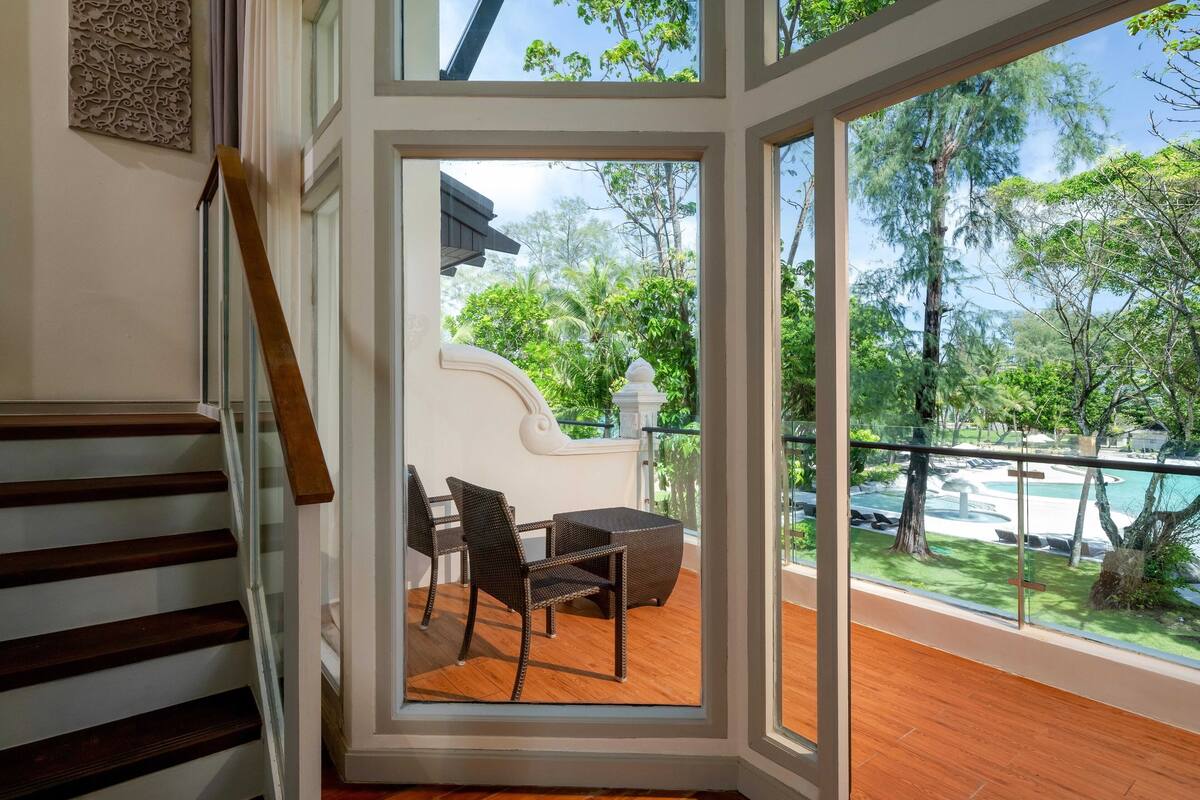 Ein modernes Interieur mit einer Holztreppe, einem Essbereich mit Korbmöbeln und Blick auf Pool und Grünfläche.