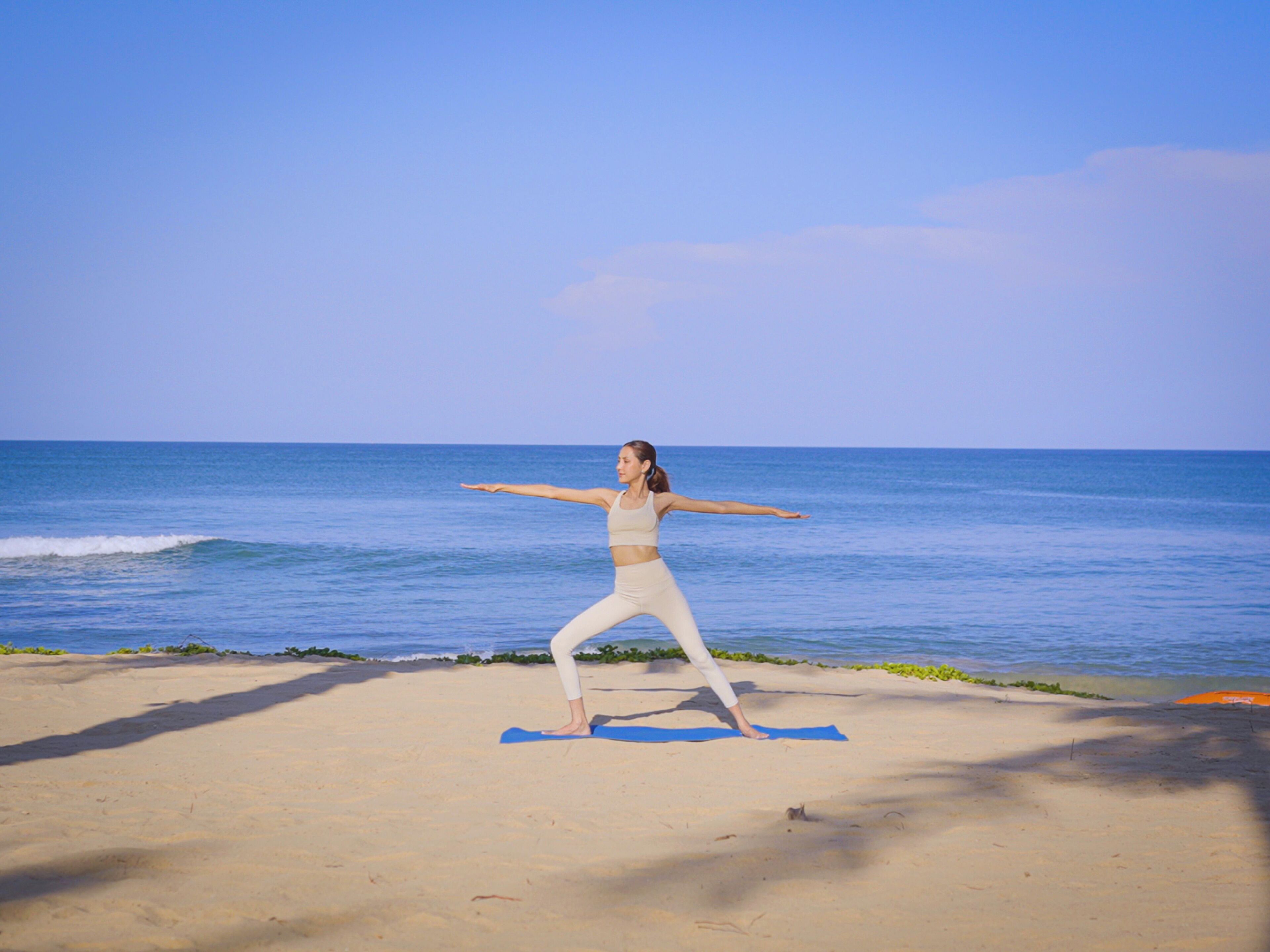 Una persona practicando yoga en una playa, con el océano al fondo.