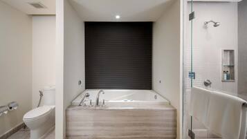 A modern bathroom with a large bathtub, a toilet, and a glass-enclosed shower area.