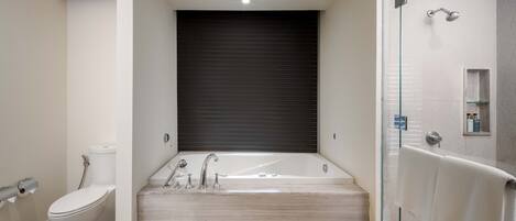 A modern bathroom with a large bathtub, a toilet, and a glass-enclosed shower area.
