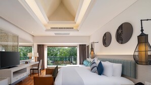 Une chambre d’hôtel moderne dotée d’un grand lit, d’une télévision, d’un bureau et d’un balcon offrant une vue sur les arbres.