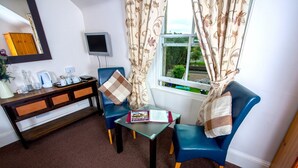 A cozy living room with a wooden cabinet, a television, and two blue armchairs with patterned cushions. - The Old Rectory Inn (Callander)