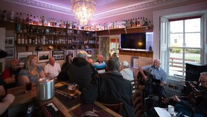 A bar with a chandelier, shelves of bottles, and a TV. - The Old Rectory Inn (Callander)