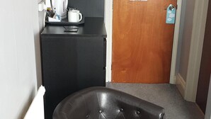 Ein kleines Hotelzimmer mit einer schwarzen Couch, einer kleinen Küchenzeile und einer Holztür mit einem Hinweisschild.