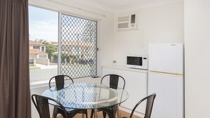 A dining area with a glass table and metal chairs, a white refrigerator, a microwave, and a view through a window with a metal screen. - Sunshine Beach Resort (Miami)