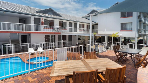 A poolside area with a wooden table and chairs, a fenced swimming pool, and a building with balconies. - Sunshine Beach Resort (Miami)