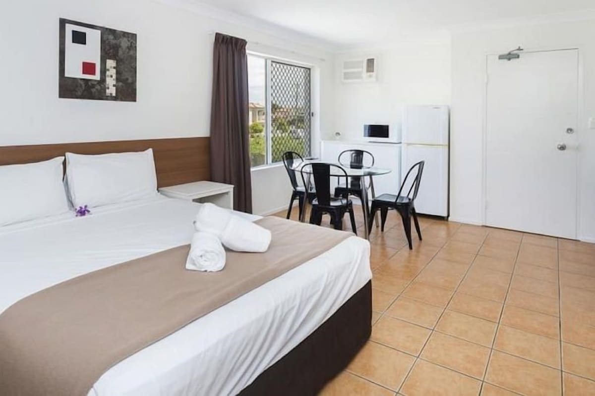 A hotel room with a bed, a desk, a chair, a TV, and a door.