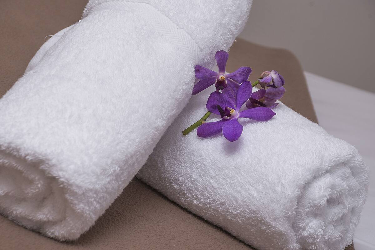 A neatly folded white towel with a purple orchid placed on top.