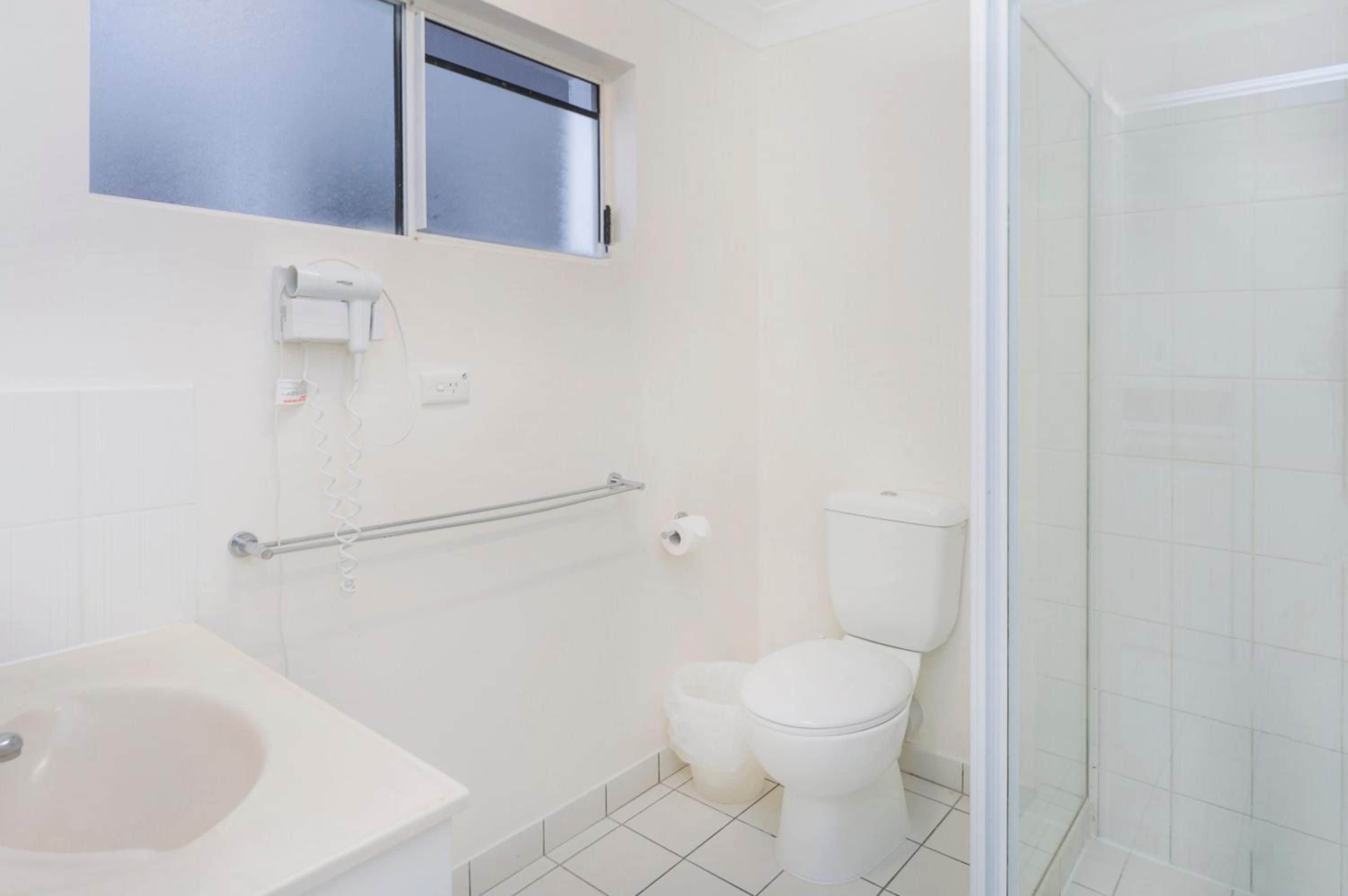 A bathroom with a toilet, a hand dryer, and a shower.