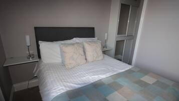 A neatly made bed with a checkered bedspread, two bedside tables with lamps, and a door leading to a closet.