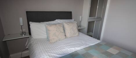 A neatly made bed with a checkered bedspread, two bedside tables with lamps, and a door leading to a closet.