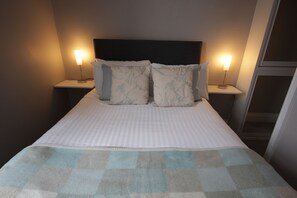 Een netjes opgemaakt bed met een geruit plaid, twee bedlampen en bijpassende kussens.