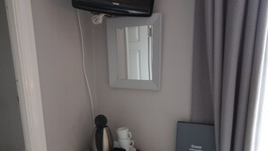 A compact room with a desk, a flat-screen TV mounted on the wall, a small table with a coffee maker, a cup, and a guest book. - The Tradesmans Arms (Buckfastleigh)