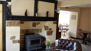 A cozy living room with a stone fireplace, a leather sofa, and a dining area with wooden furniture. - The Tradesmans Arms (Buckfastleigh)