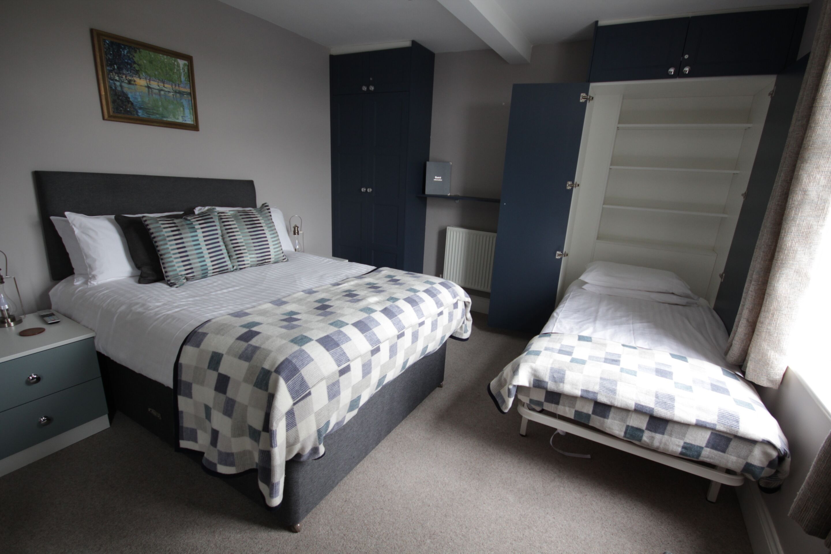 A bedroom with a large bed, a smaller bed, a nightstand, a dresser, and a radiator.