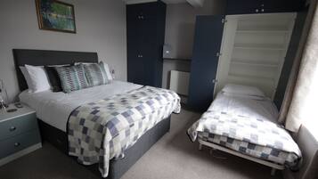 A bedroom with a large bed, a smaller bed, a nightstand, a dresser, and a radiator.