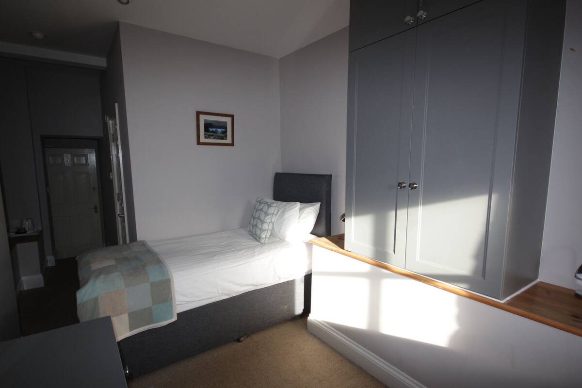 A bedroom with a bed, a wardrobe, a small table, and a picture on the wall.