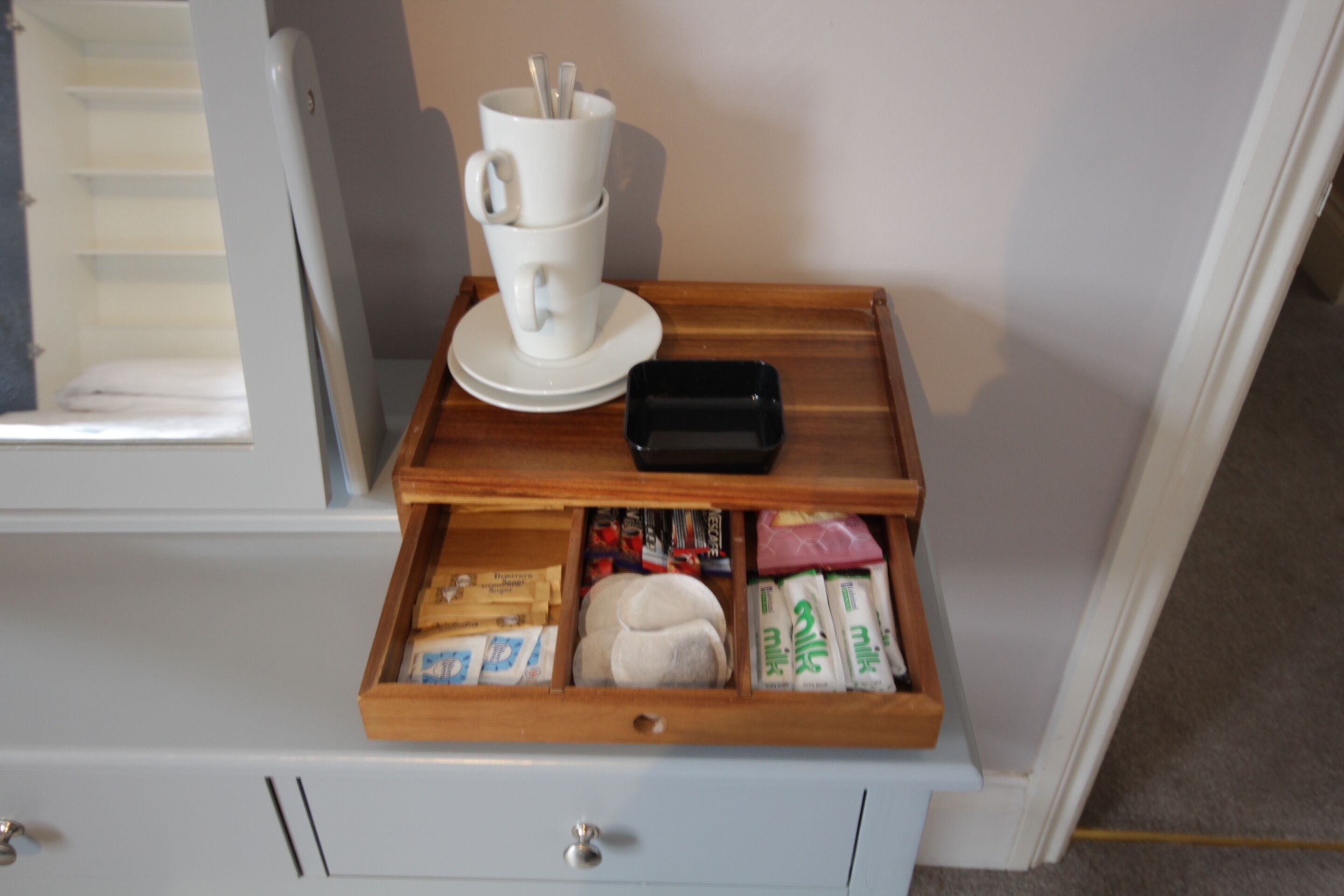 A drawer with a cup and saucer, a black object, and various packaged items.