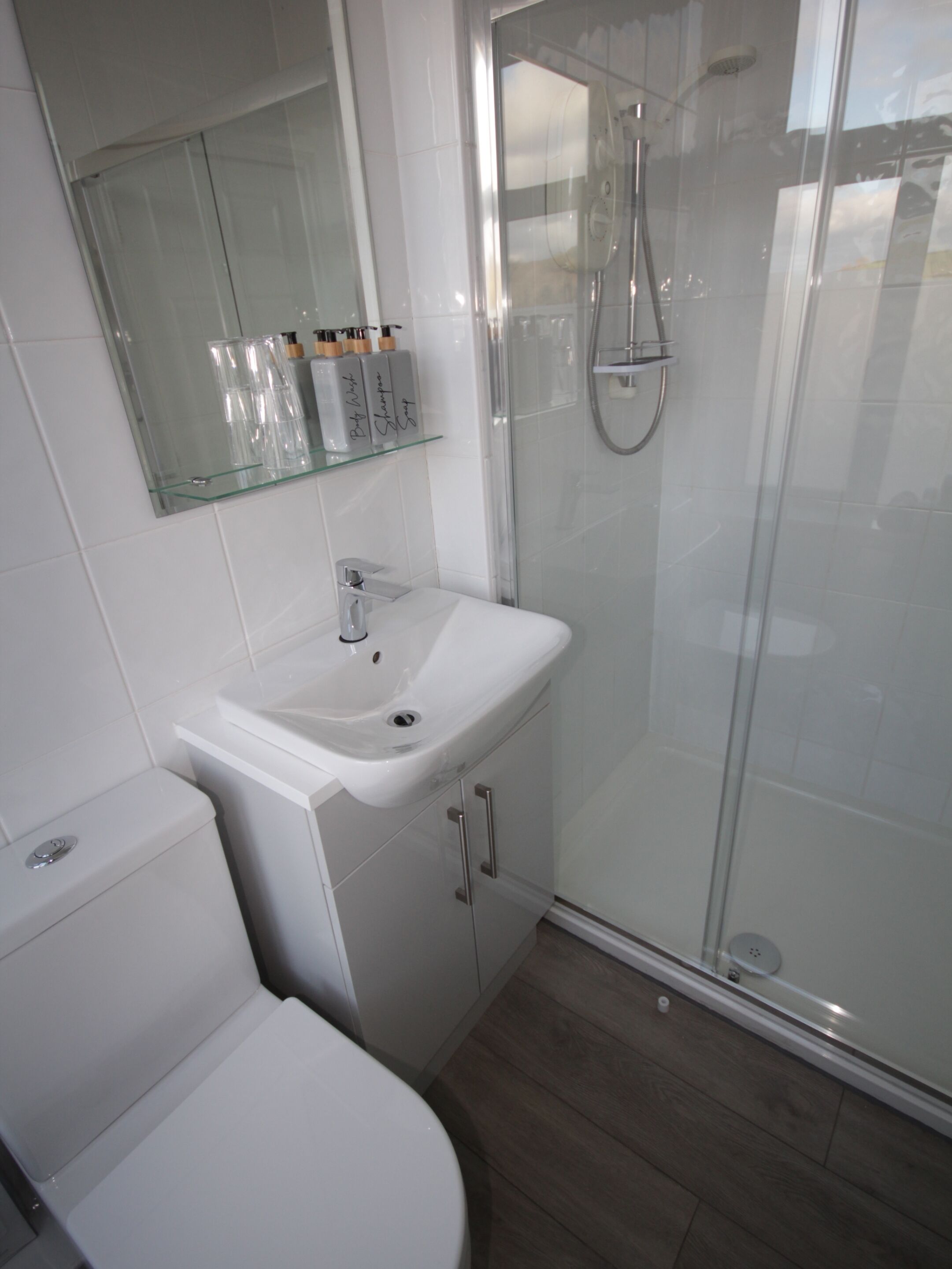 Un baño moderno con cabina de ducha de vidrio, un lavamanos blanco y un inodoro.