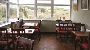 A dining area with wooden tables and chairs, large windows with a view of a green landscape. - The Tradesmans Arms (Buckfastleigh)