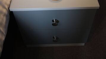 A white bedside table with a lit Edison bulb lamp, a wooden knob, and two drawers.