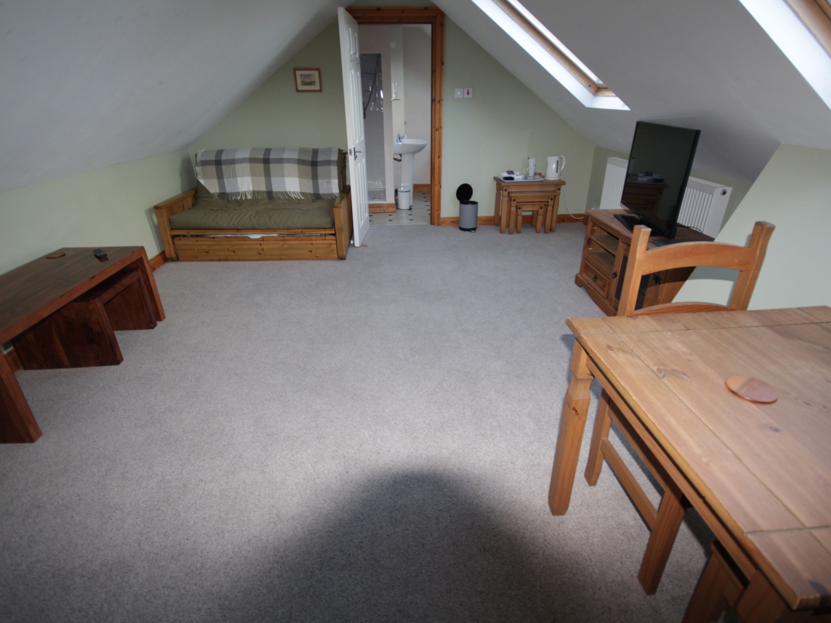 A small attic room with a loft bed, a wooden table, and a television.