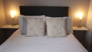 A neatly made bed with a striped bedspread, two bedside tables with lamps, and a dark headboard. - The Tradesmans Arms (Buckfastleigh)