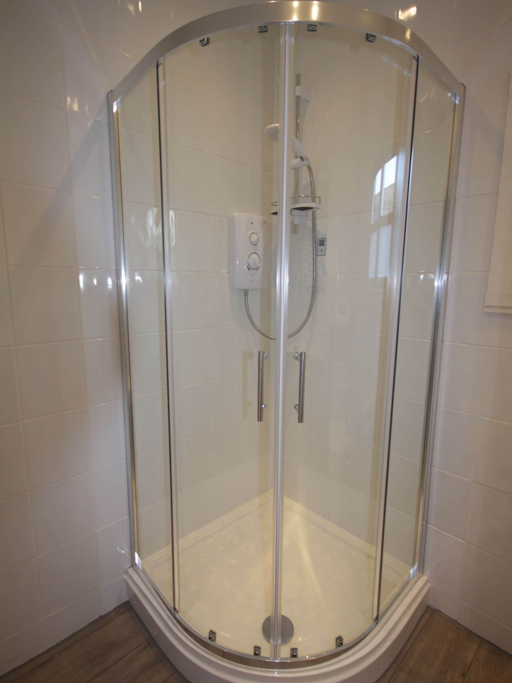 Ducha con cerramiento de vidrio, panel de control y cabezal de ducha manual.