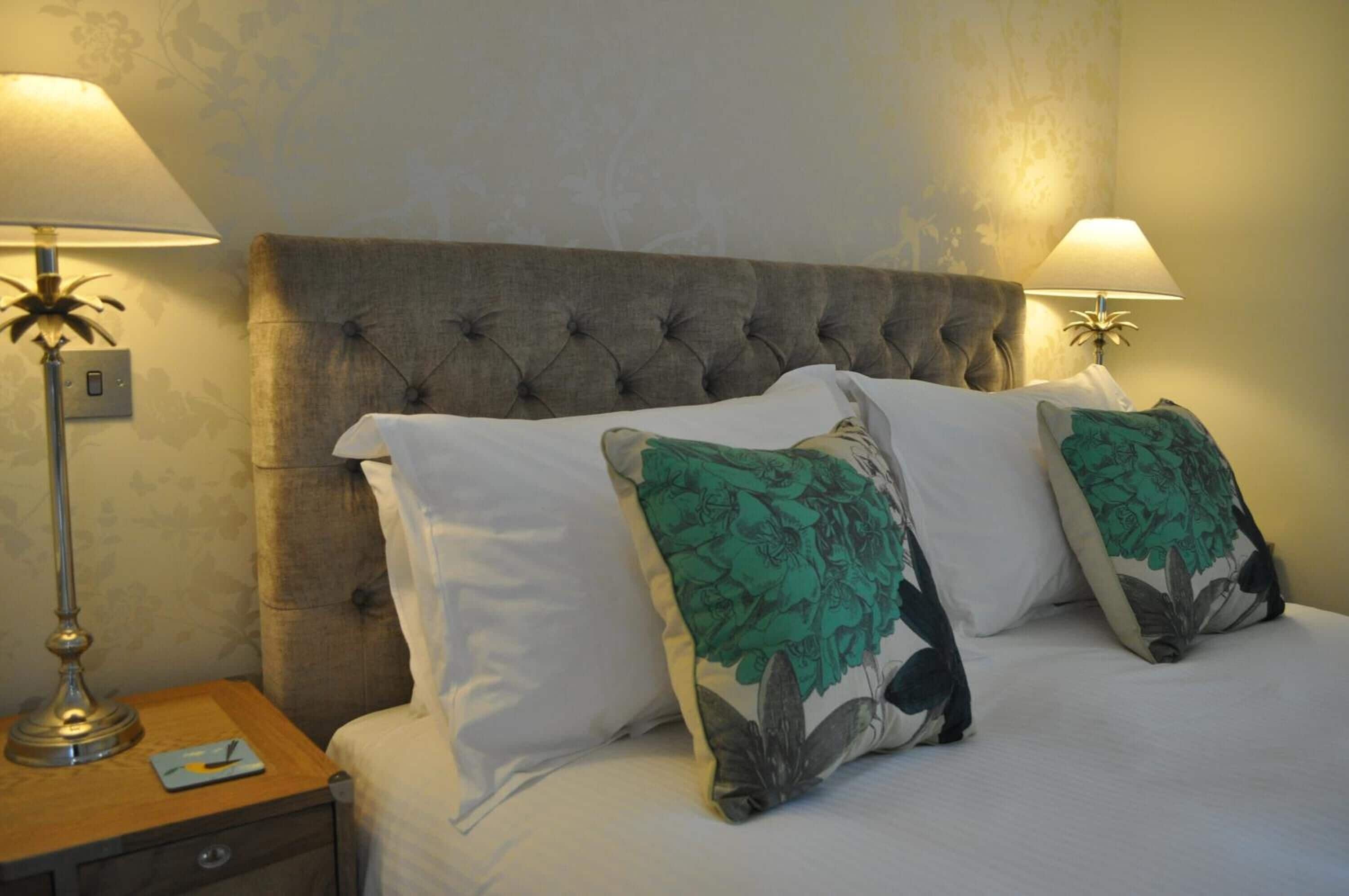 A neatly made bed with a tufted headboard, two bedside lamps, and floral-patterned pillows.