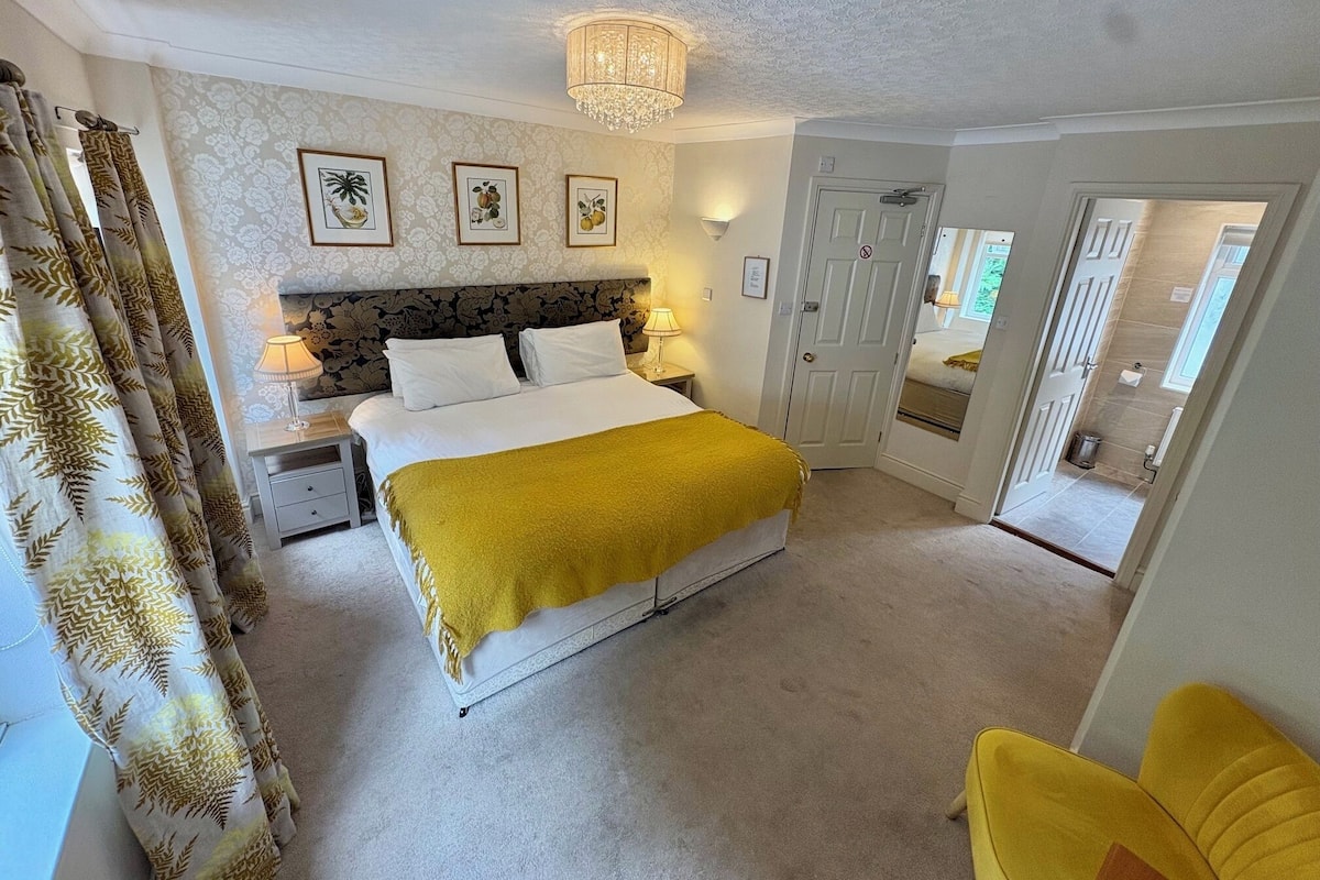 A bedroom with a bed, bedside tables, a chandelier, and a door leading to another room.