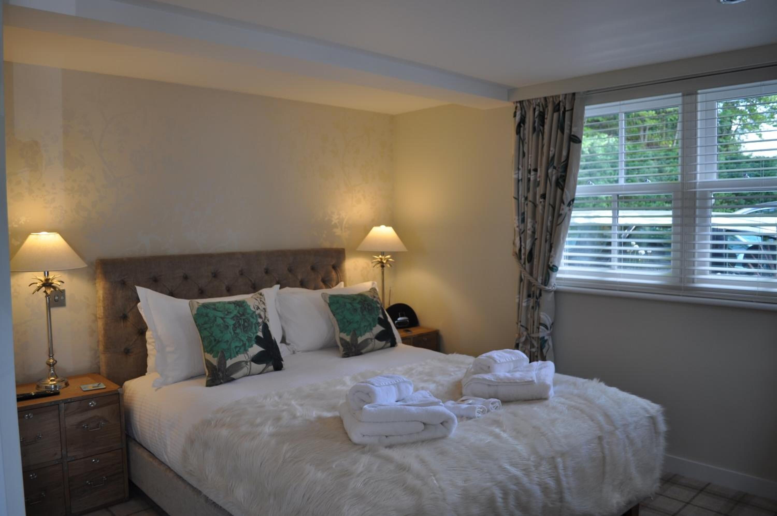 A neatly made bed with two pillows, a nightstand with a lamp, and towels on the bed.