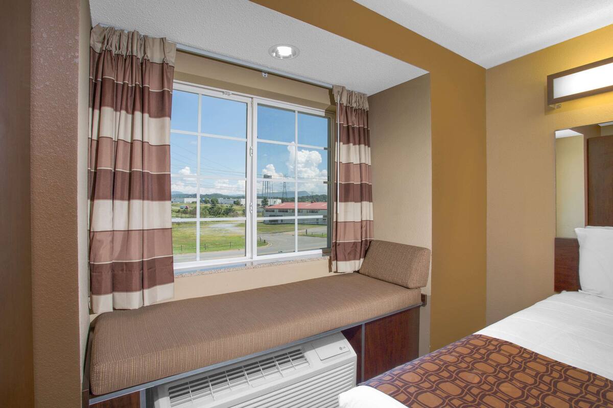 A hotel room with a large window, a bench, and a bed.