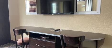Un comedor con una mesa larga, dos sillas, un televisor montado en la pared y un espejo sobre la mesa.