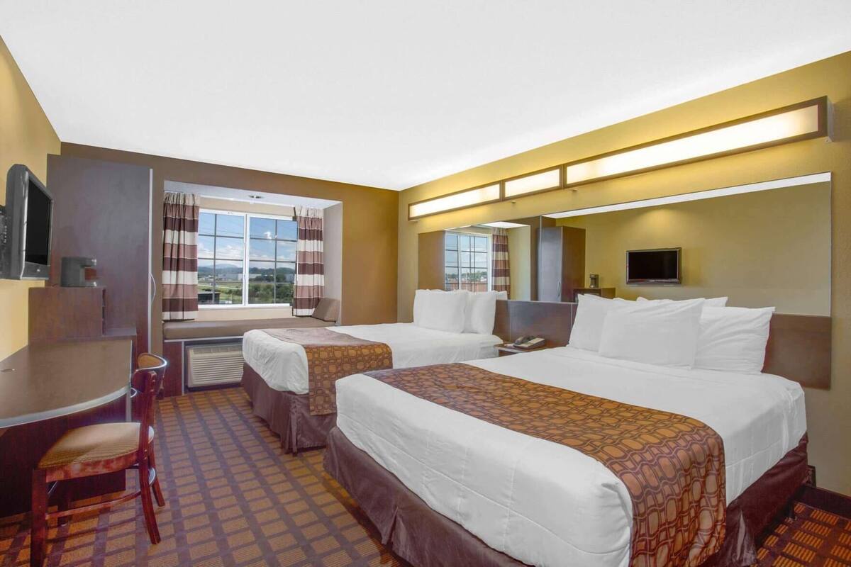 A hotel room with two beds, a desk, a chair, a TV, and a window with curtains.