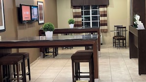 A hotel dining area with a long table, multiple chairs, a small potted plant, and a TV mounted on the wall. - Microtel Inn & Suites by Wyndham Harrisonburg (Harrisonburg)