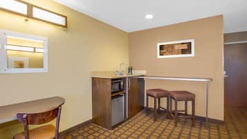 Cocina compacta con microondas, lavabo y dos taburetes.