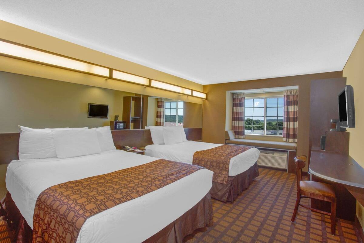 A hotel room with two beds, a desk, a TV, and a window with a view.