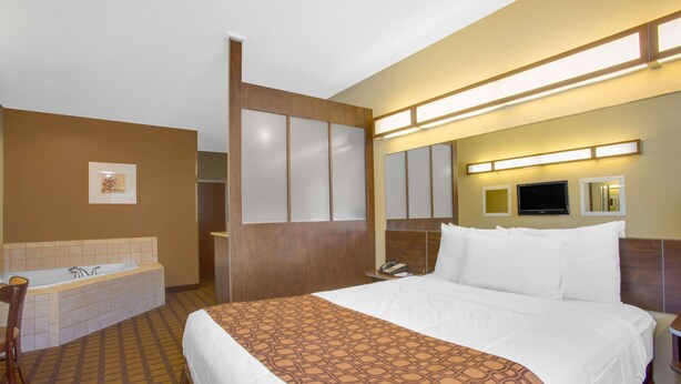 A hotel room with a large bed, a separate bathroom with a bathtub, a desk with a chair, and a flat-screen TV mounted on the wall. - Microtel Inn & Suites by Wyndham Harrisonburg (Harrisonburg)