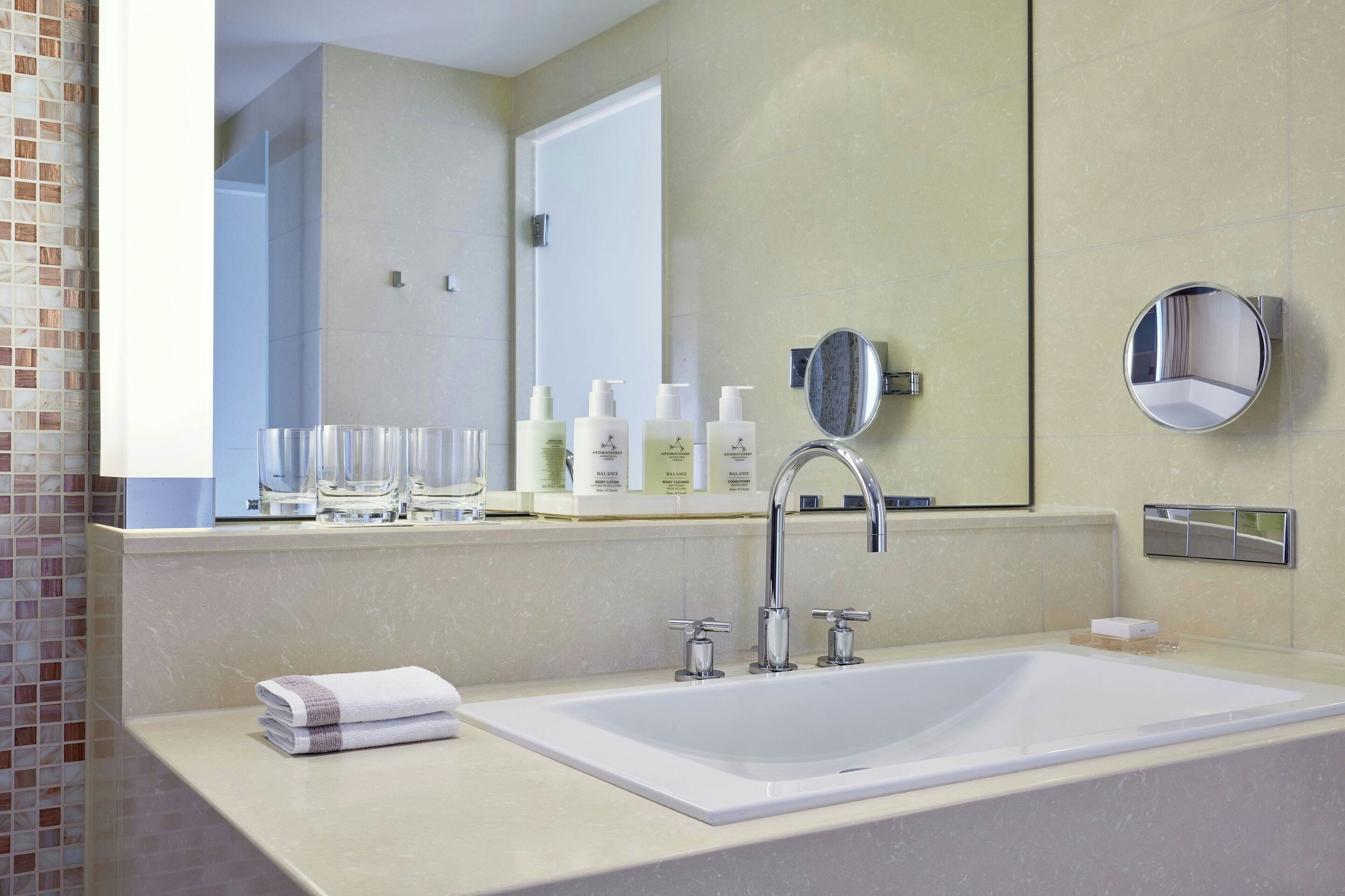 Un bagno moderno con un lavandino grande, due rubinetti, uno specchio e articoli da toilette sul ripiano.