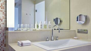 Un bagno moderno con un lavandino grande, due rubinetti, uno specchio e articoli da toilette sul ripiano.