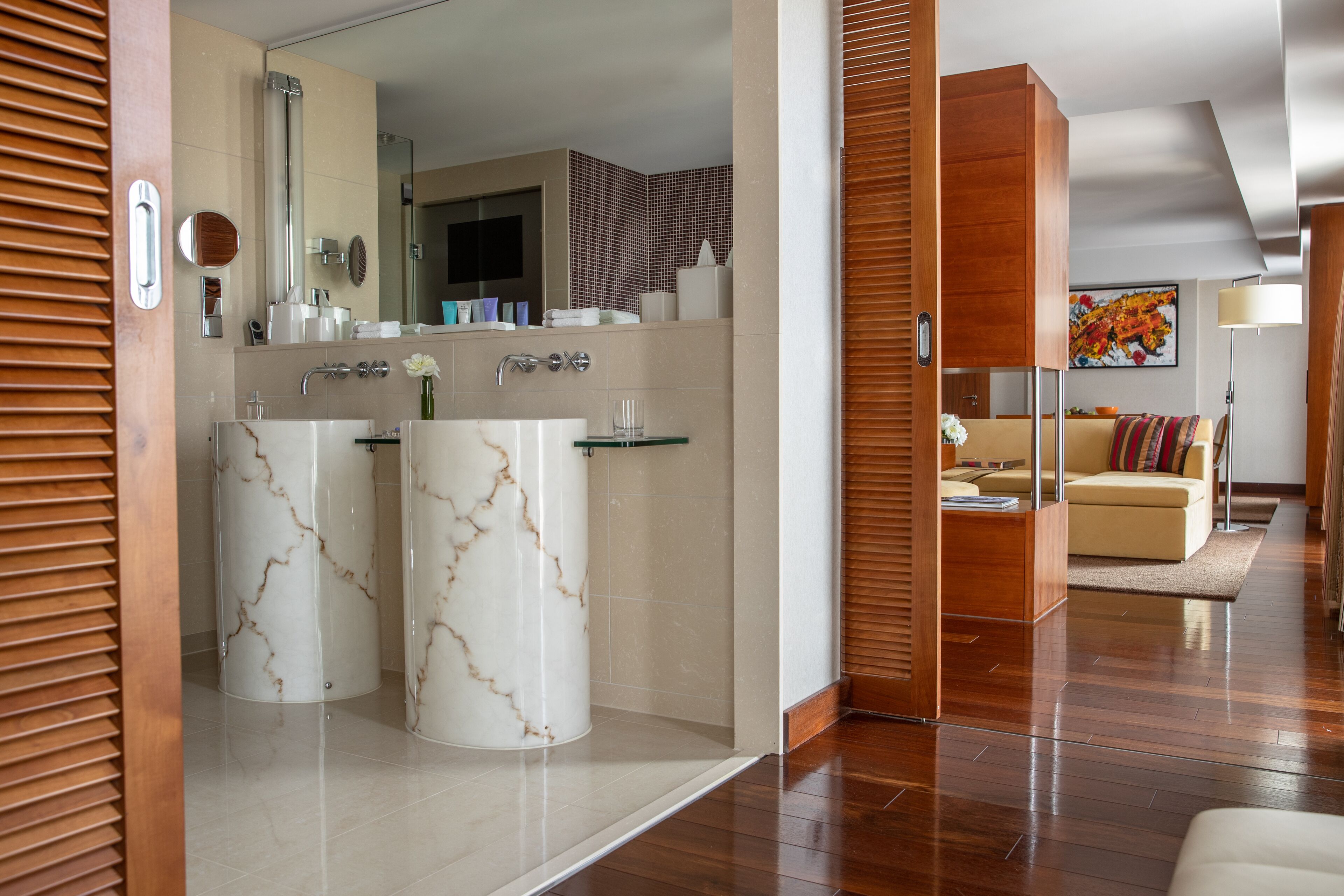 Een moderne badkamer met twee marmeren wastafels, een grote spiegel en een douchegedeelte.
