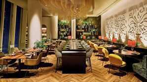A modern restaurant with a long communal table, multiple seating areas, and decorative wall panels.
