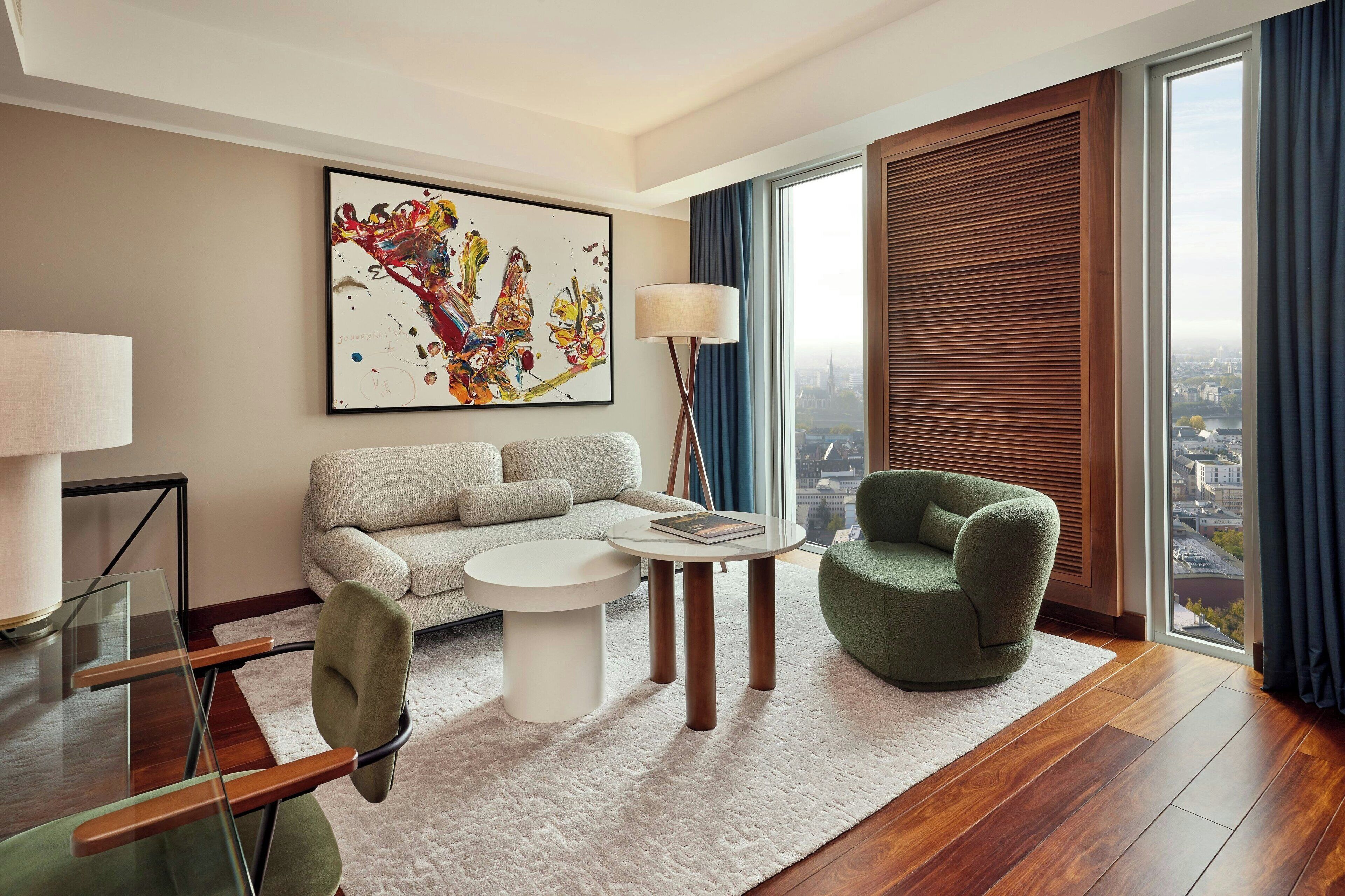 Uma sala de estar moderna com sofá, poltrona, mesa de centro e vista para a cidade através de grandes janelas.