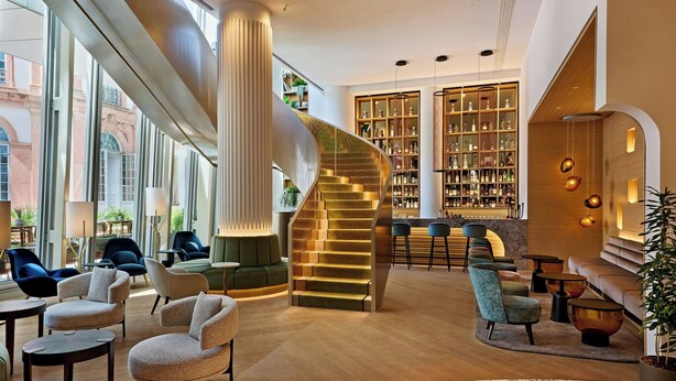 A modern lobby with a spiral staircase, seating areas, and a bar with shelves of bottles.