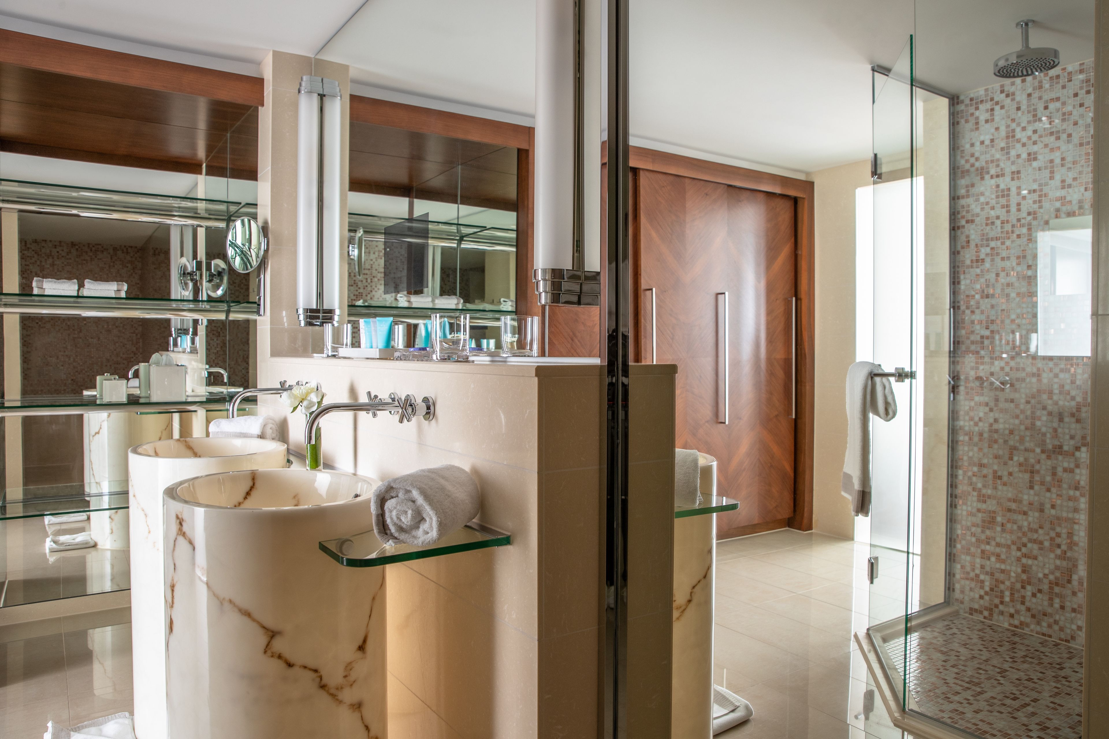 A modern bathroom with a glass shower enclosure, marble sinks, and a large mirror.