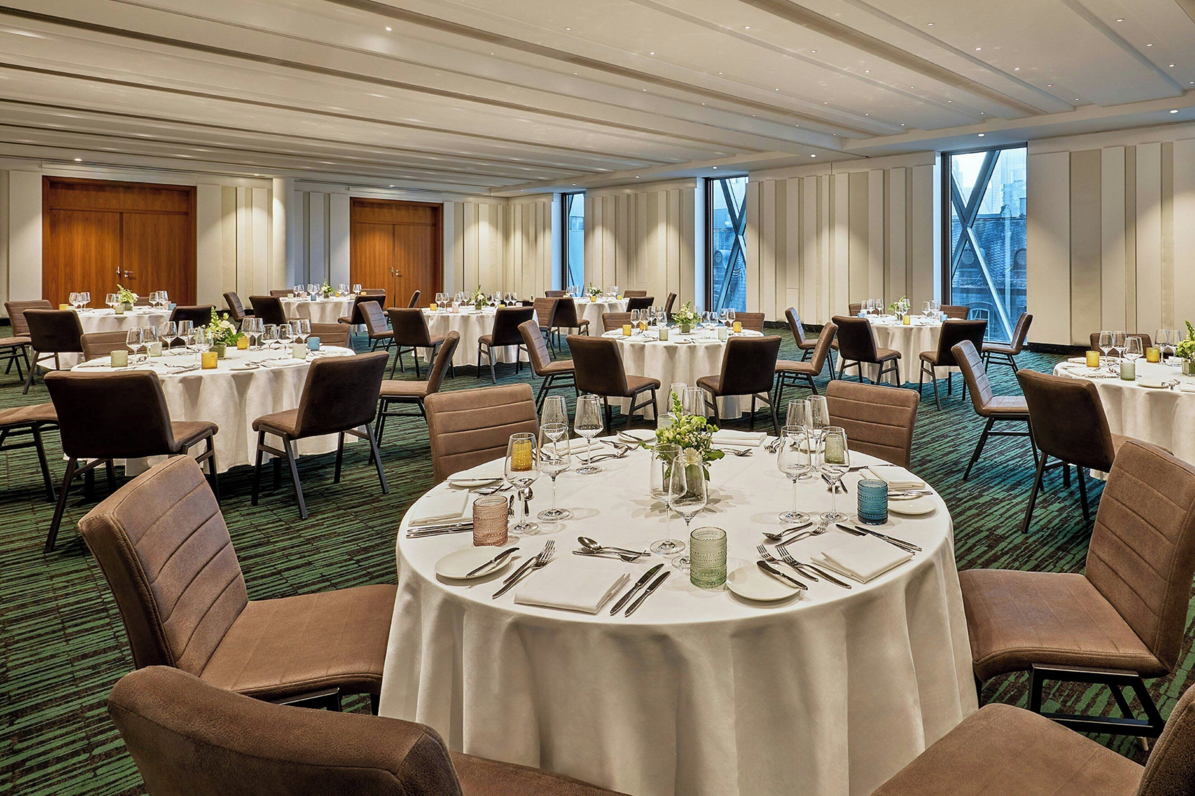 A banquet hall with round tables set for dining, featuring white tablecloths and brown chairs.